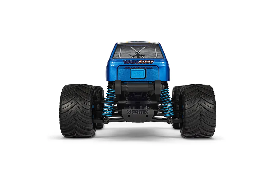 Rear view of the ARRMA Freedom Flyer Grom RC monster truck featuring a metallic blue body, black off-road tires, and blue coil-over suspension springs.