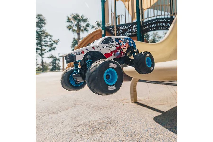ARRMA Freedom Flyer Grom RC monster truck jumping off a playground slide in a park.