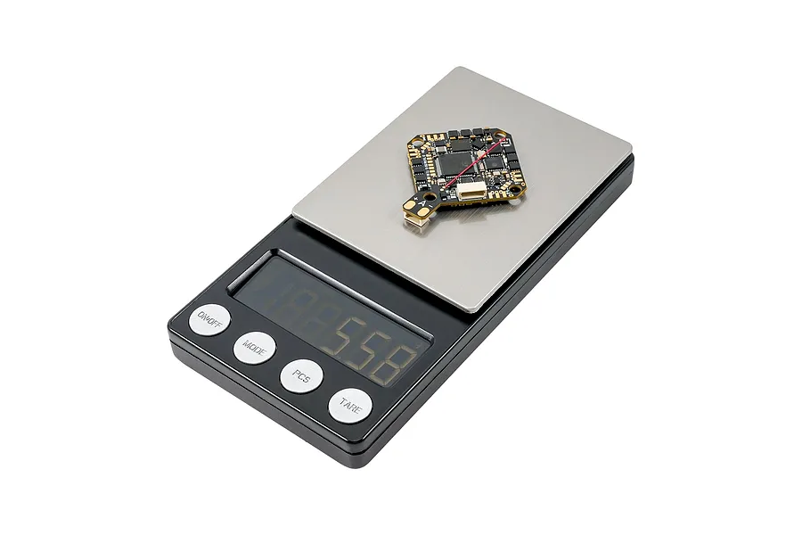 A BetaFPV flight controller circuit board resting on a digital weighing scale.