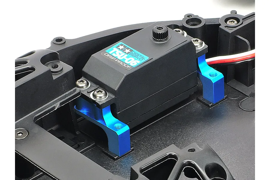 A Tamiya TSU-06 digital servo mounted to a black RC chassis using two bright blue anodized aluminium servo stays.