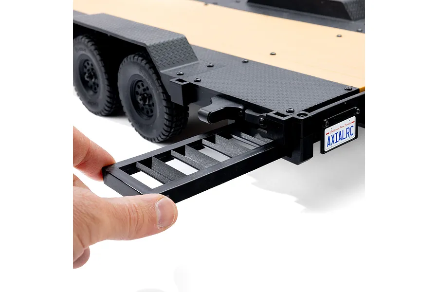 A hand pulling out a black plastic loading ramp from the rear of an Axial 1/10 scale flat bed RC trailer.