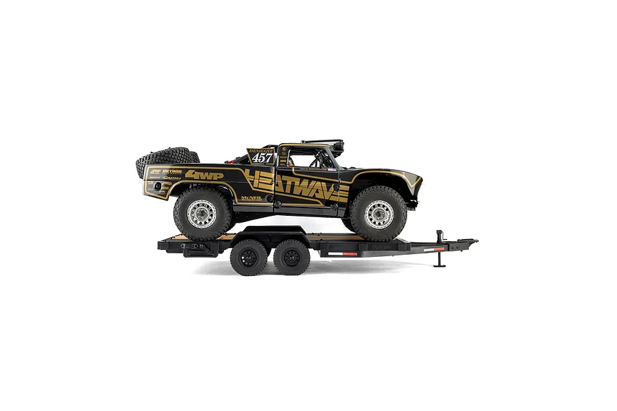 An Axial 1/10 scale flat bed vehicle trailer carrying a black and gold Heatwave RC trophy truck against a white background.