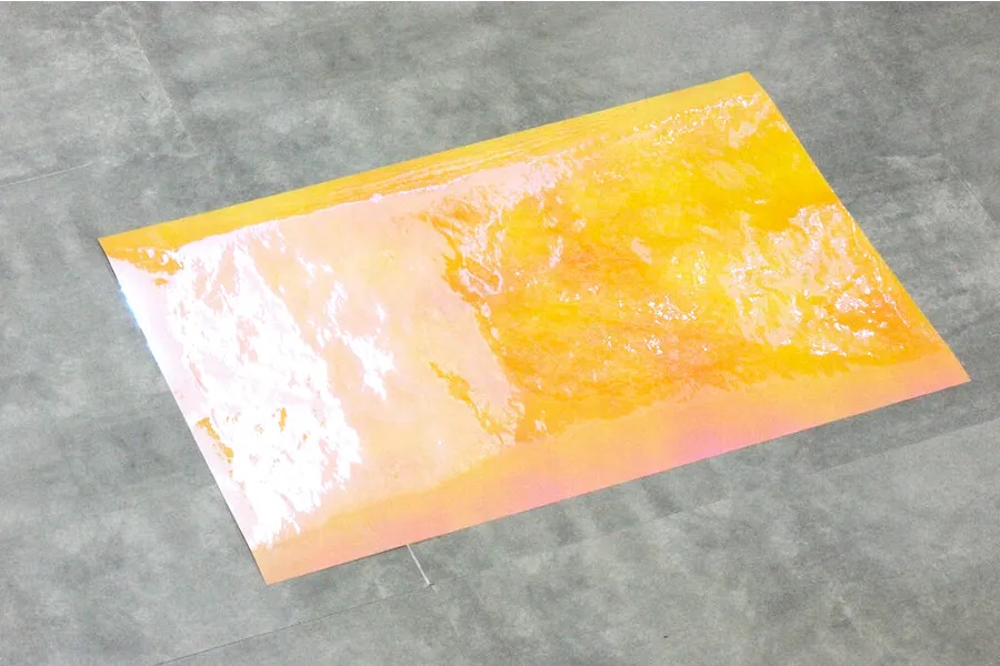 A rectangular sheet of yellow Aurora window sticker film with a reflective, iridescent texture laid on a grey surface.