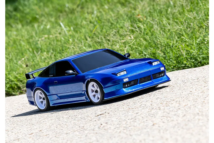 A blue Traxxas 4-Tec 2.0 Nissan 240SX RC drift car driving on a paved surface with a grassy background.