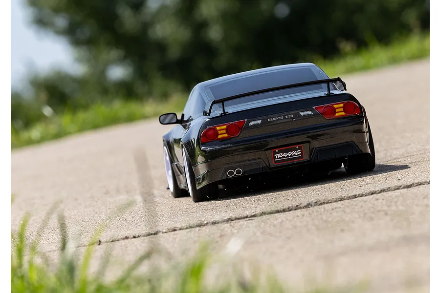Rear view of a black Traxxas Nissan 240SX RC drift car driving on a paved road with a blurred green background.
