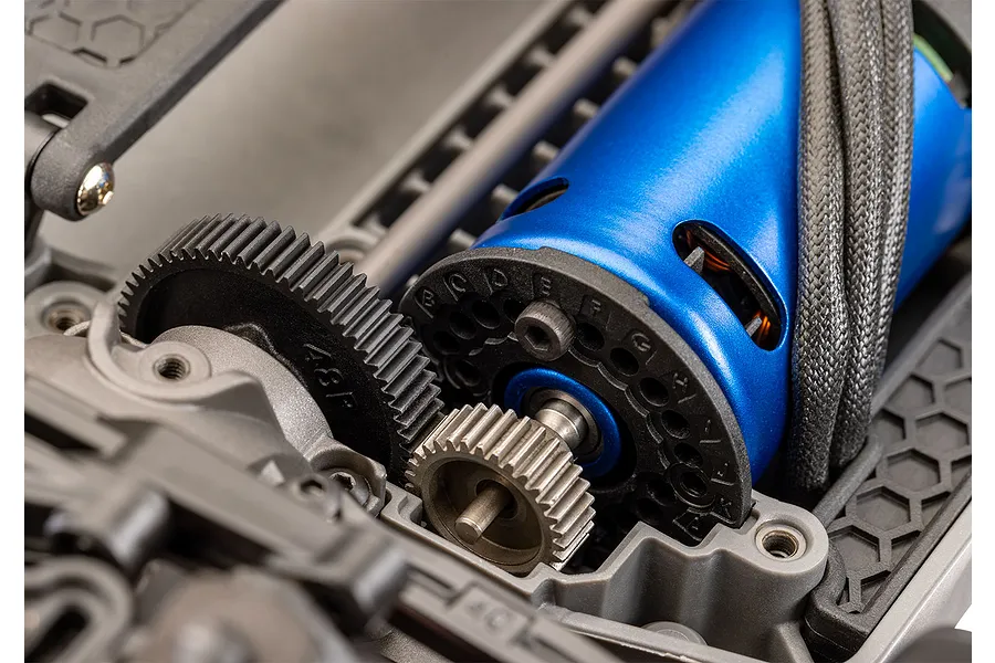 Close-up of a blue electric RC motor and black plastic spur gear mounted on a grey composite chassis.