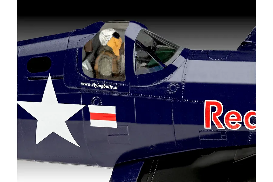 Close-up of a painted plastic model F4U-4 Corsair cockpit showing a pilot figure, dark blue fuselage, white star insignia, and Red Bull branding.