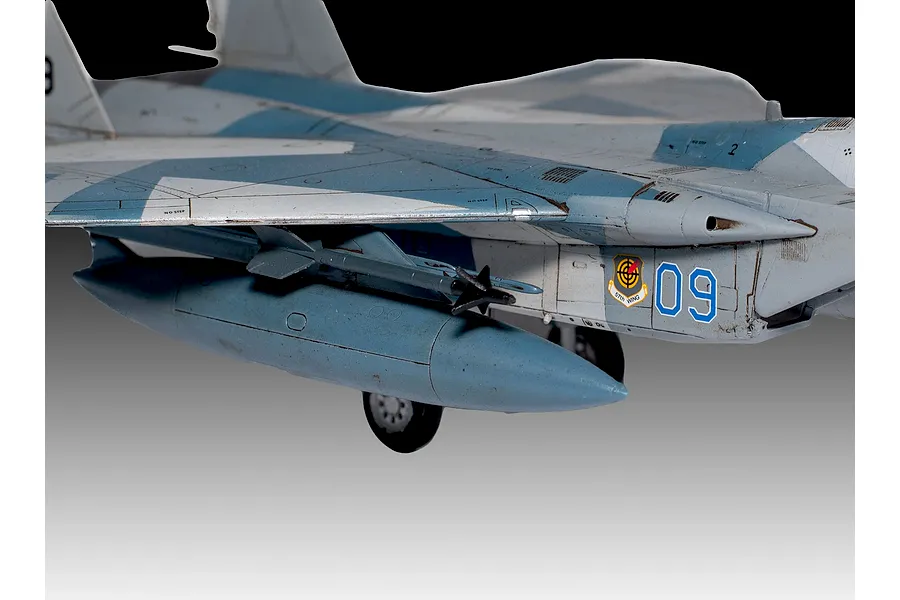 Close-up of a painted plastic model F-15C Eagle fighter jet showing the fuselage, wing, external fuel tank, and 57th Wing emblem.