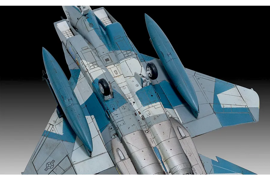 A high-angle view of the underside of a painted and weathered F-15C Eagle model aircraft, showing landing gear, fuel tanks, and blue-grey camouflage.