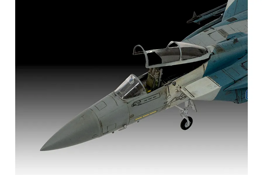 Close-up of a 1/72 scale plastic model F-15C Eagle fighter jet, showing the cockpit area, nose, and landing gear against a gradient background.