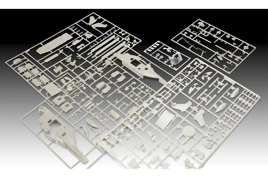 Several light grey plastic model kit sprues for a helicopter model, including fuselage halves and small components, arranged on a dark background.