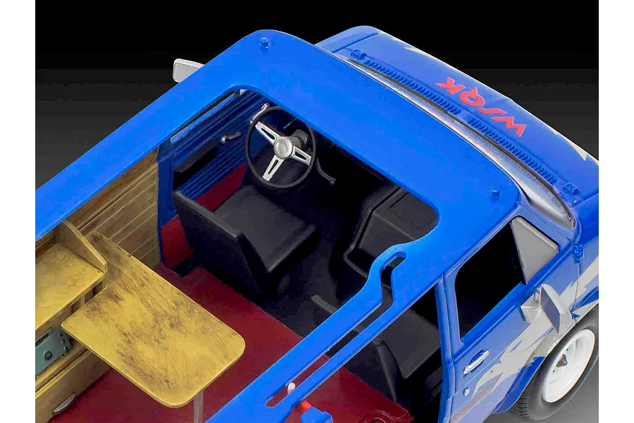 High-angle view of the interior of a blue Revell Stranger Things Squawk Van model kit showing the driver seat, steering wheel, and wooden work desk.