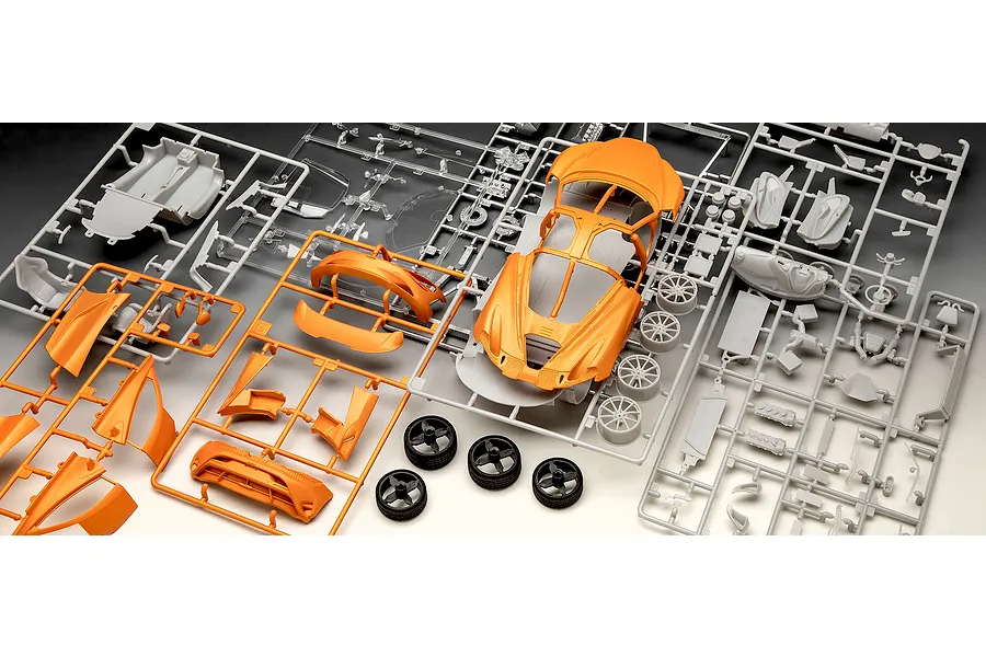 Plastic model kit parts for a Revell 1/24 McLaren 750S, including orange body panels, grey chassis components, and black rubber tires on sprues.