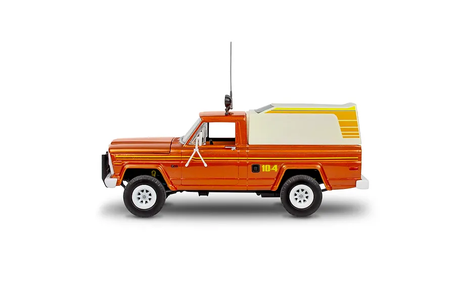 Side view of a 1/24 scale Revell Jeep J-10 pickup truck model with a camper shell, painted metallic orange with yellow stripes.