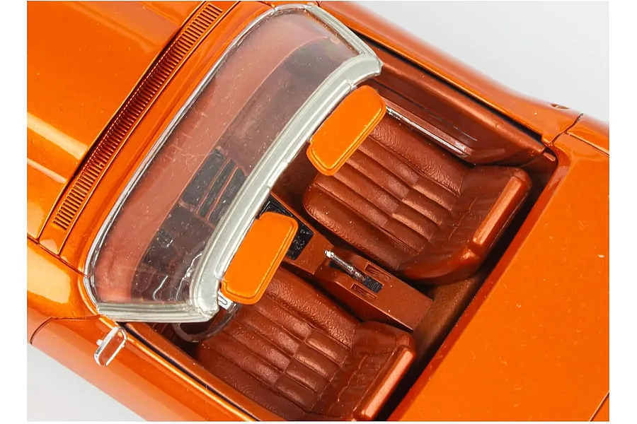 Top-down view of the interior of a metallic orange scale model Corvette showing bucket seats, center console, and windshield frame.