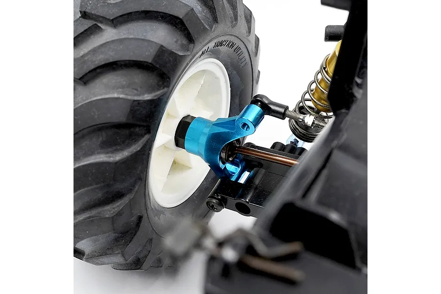 Close-up of a blue anodized aluminium RC car steering hub installed on a vehicle with a black rubber tyre and white wheel rim.