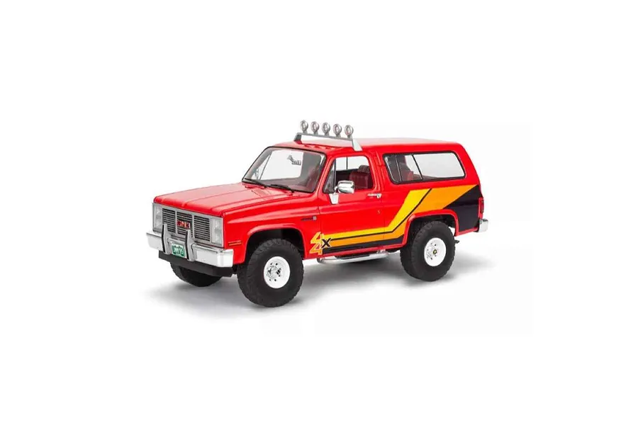 A 1/25 scale model of a red 1985 GMC Jimmy High Roller SUV with yellow and black side decals and a roof-mounted light bar.
