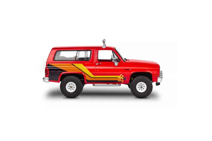 Side view of a red 1/25 scale Revell '85 GMC Jimmy High Roller plastic model kit with yellow and black side decals and white wheels.
