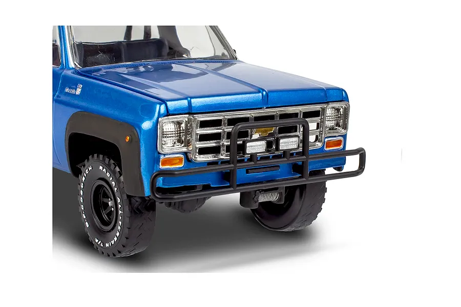 Close-up of the front end of a blue 1978 Chevy pickup model kit with a black brush guard and off-road tires.