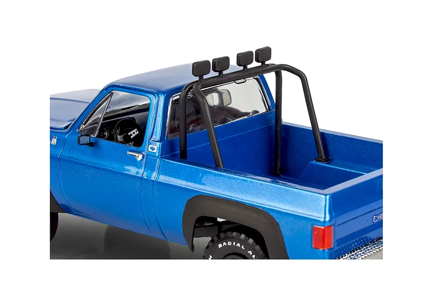 A close-up view of a blue 1978 Chevy 4x4 model truck featuring a black roll bar with four off-road lights mounted in the truck bed.
