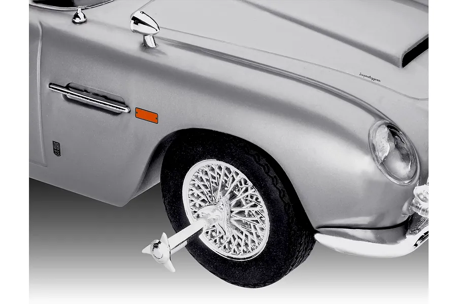 Close-up of the front fender and wheel of a silver Aston Martin DB5 model car, featuring a wire-spoke wheel with a tire slasher accessory.