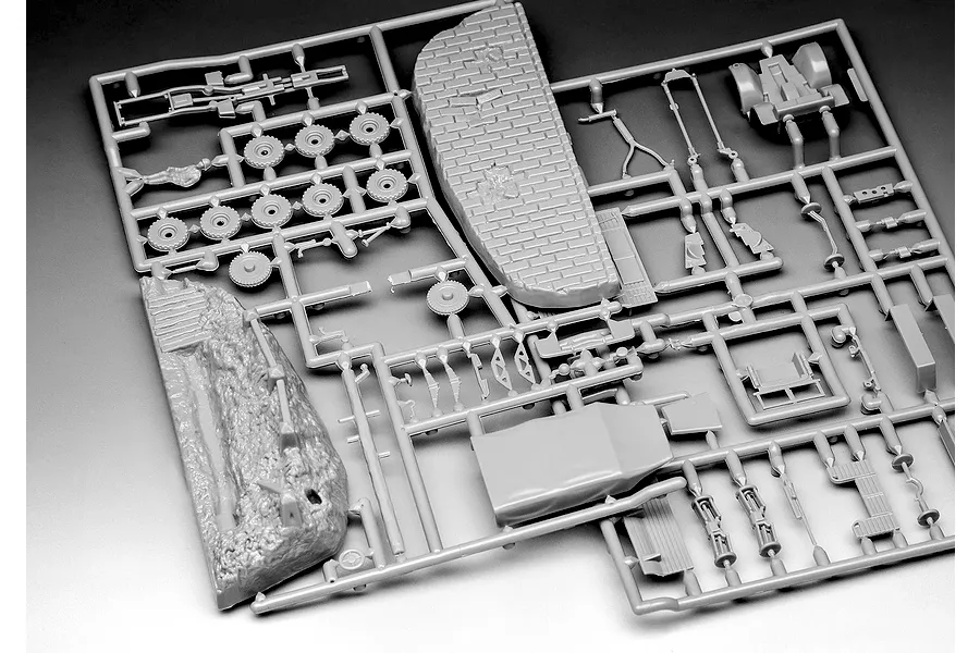 A grey plastic sprue containing various model kit parts including wheels, a brick wall section, and terrain base for a Revell military model kit.