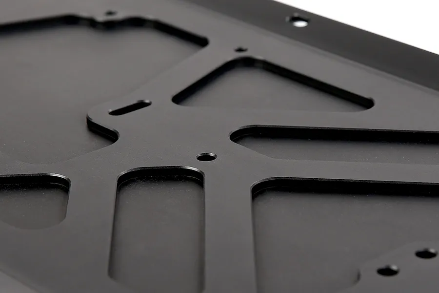 Close-up of a black anodized aluminium RC main chassis plate with machined cutouts and mounting holes.