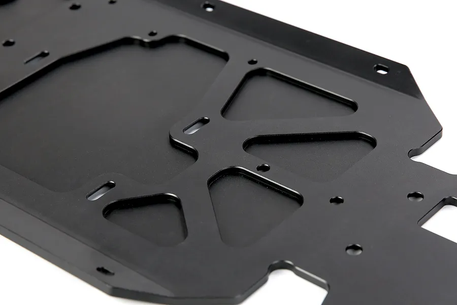 A close-up view of a black anodized aluminium RC main chassis plate with various mounting holes and cutouts.