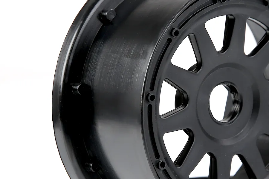 A close-up view of a black plastic RC short course rear wheel rim against a white background.