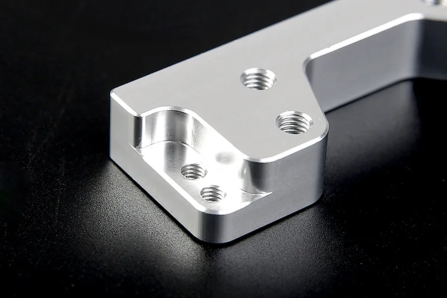 Close-up of a silver Rovan aluminium engine mount showing machined edges and threaded screw holes against a black background.