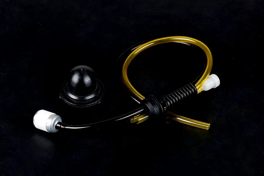 Rovan Baja fuel system kit including fuel filter, black and yellow fuel tubing, rubber grommet, and a black tank cap seal on a dark background.