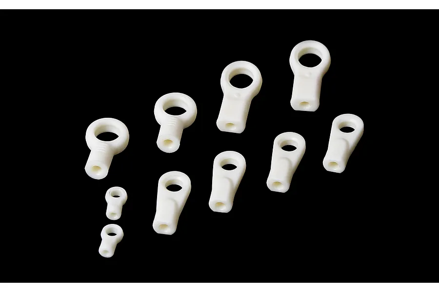 A collection of ten white plastic RC rod ends of varying sizes arranged on a black background.