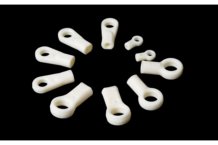 A collection of white plastic RC ball ends of various sizes arranged in a circle against a black background.