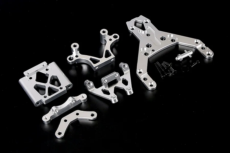 A set of silver aluminium RC front bulkhead components and an upper plate with mounting hardware on a black background.
