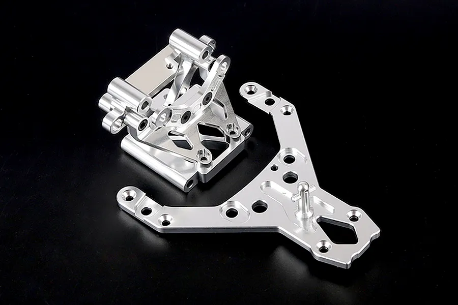 A silver aluminium front bulkhead assembly and matching upper plate for an RC vehicle, shown against a plain black background.