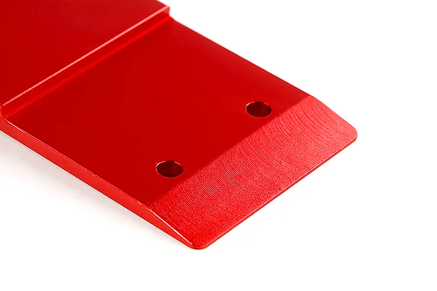 A close-up view of a red anodized aluminium front skid plate for an RC car, showing the angled edge and mounting holes.