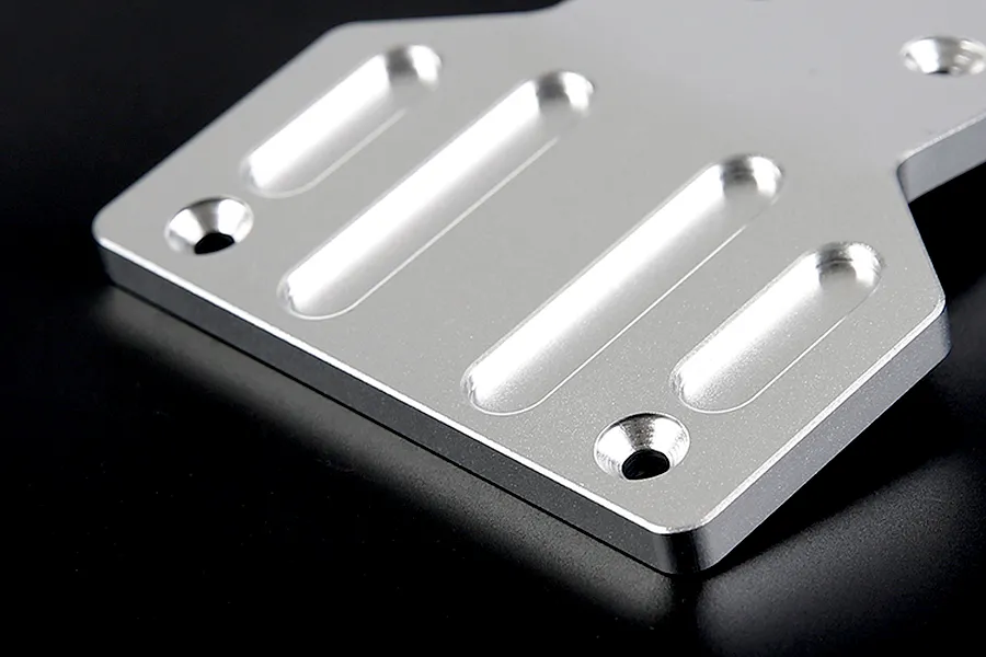 A close-up view of a silver aluminium front skid plate for an RC vehicle, featuring machined slots and countersunk screw holes.