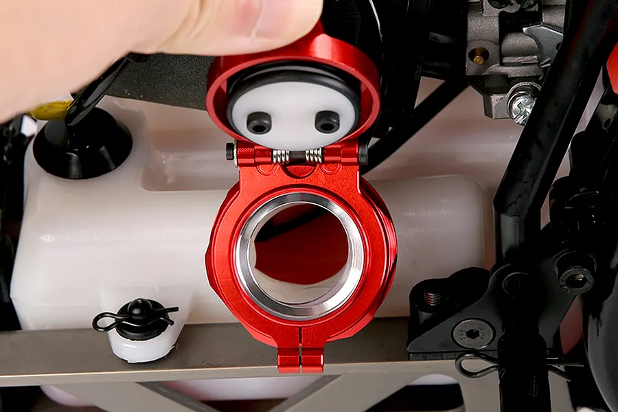 A close-up view of a red Rovan aluminium fuel tank cap being held open, revealing the white plastic fuel tank underneath on an RC vehicle.