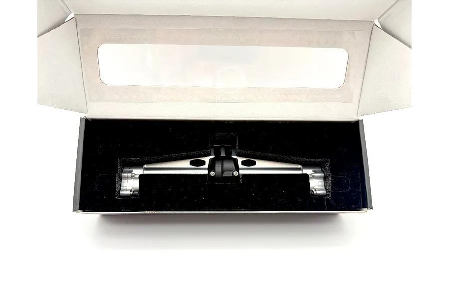 Silver aluminium RC axle housing in a cardboard box with black foam insert.