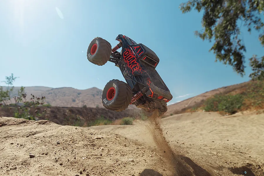 ARRMA Quake Grom RC monster truck launching off a dirt ramp into the air under a clear blue sky