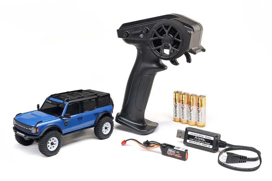 Axial SCX30 blue Ford Bronco RC rock crawler with Spektrum transmitter, LiPo battery, USB charger, and AA batteries on a white background.