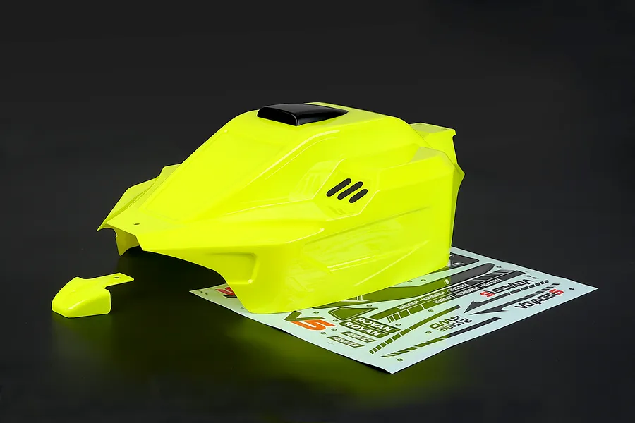 Bright yellow painted RC buggy body shell with a sticker sheet and separate small piece on a dark background.