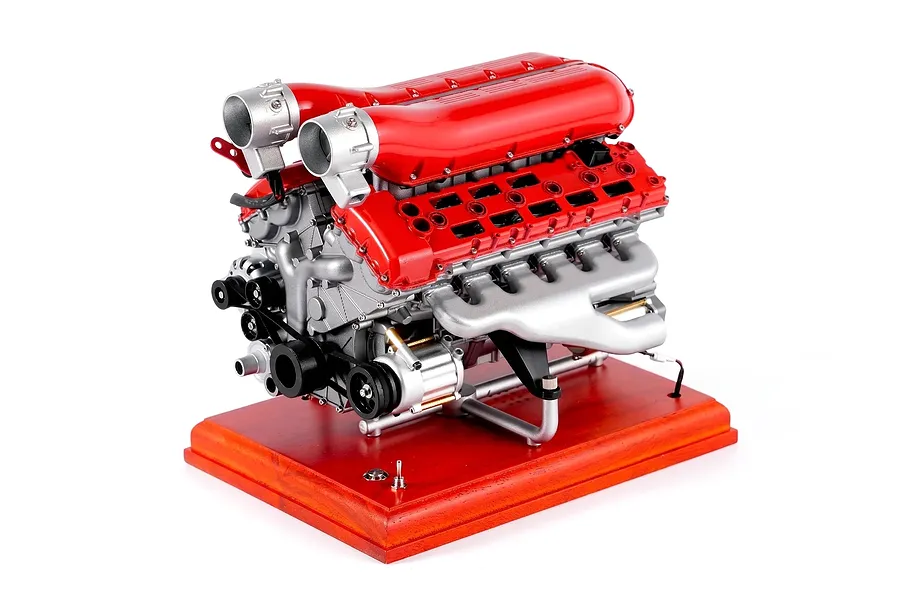 A detailed studio product shot of the Teching DM108 V12 Engine Scaled Metal Model Kit mounted on a red wooden base against a white background.