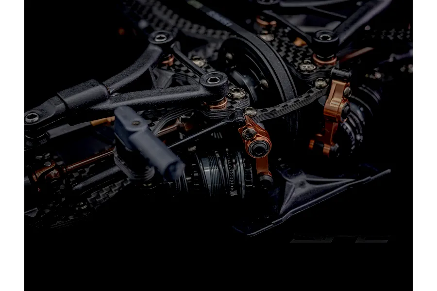 Close-up studio shot of the RC Maker SP2 touring car chassis featuring carbon fibre and bronze coloured alloy components.