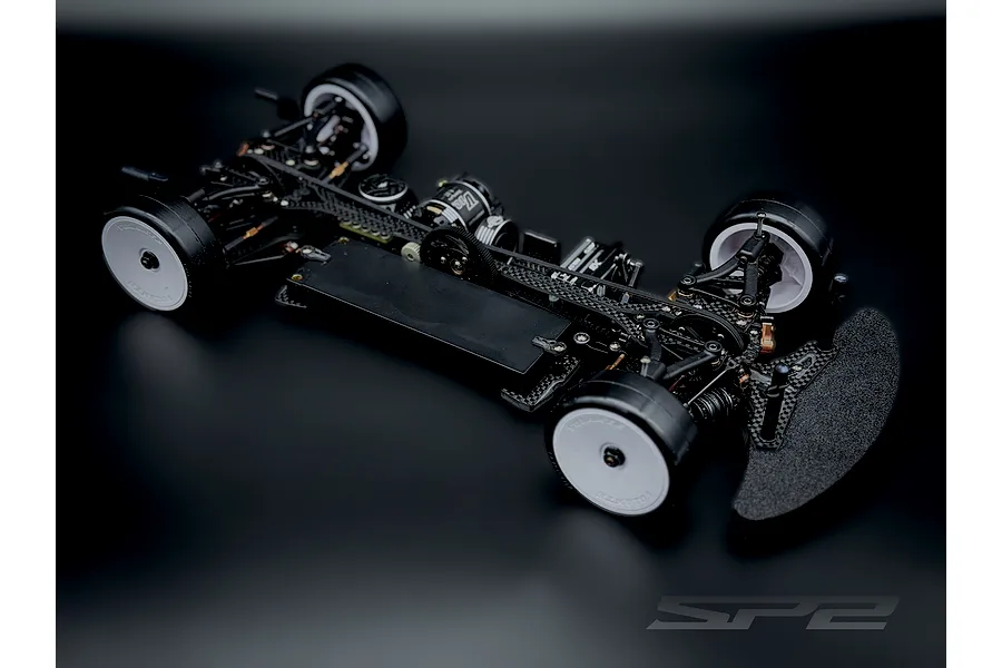 RC Maker SP2 EP 1/10 scale electric touring car chassis with carbon fibre deck and white wheels on dark background.