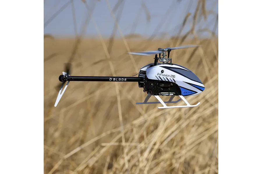 Blade InFusion 210 RC helicopter in flight outdoors against a blurry dry grass field background.