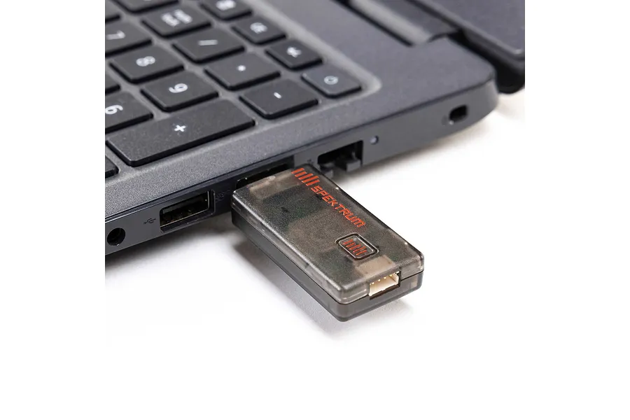 Spektrum wireless USB simulator dongle plugged into the side port of a black laptop keyboard.