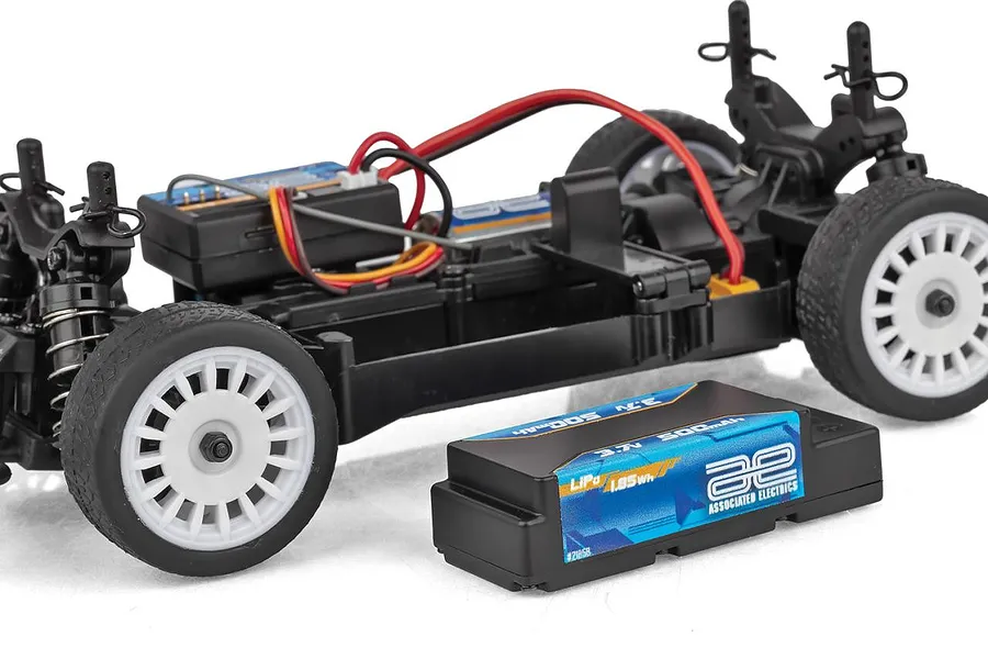 Team Associated RC24 chassis without body shell, showing black plastic frame, white wheels, and a separate LiPo battery placed alongside.