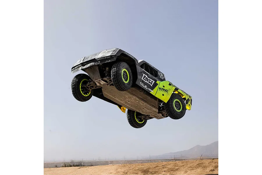 Losi 1/5 scale 5IVE-TG 3.0 petrol RC short course truck jumping high into the air above a dirt track against a clear sky.