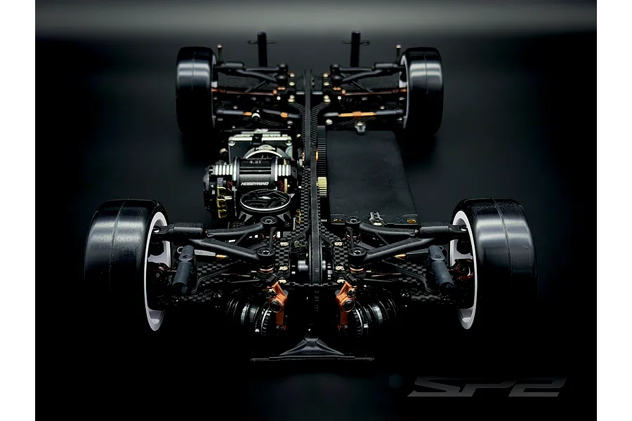 Top-down rear view of the RC Maker SP2 EP RC touring car chassis featuring carbon fiber, black components, and bronze accents on a dark background.